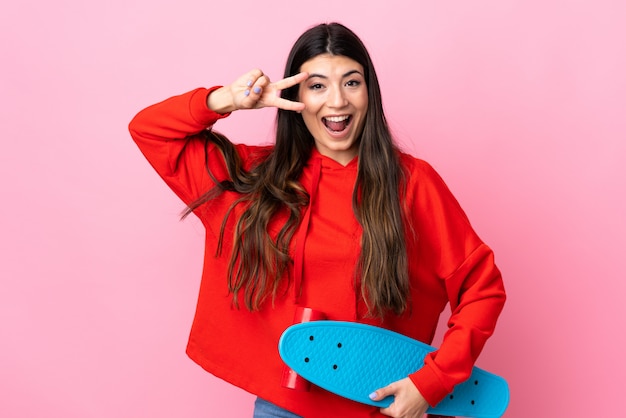 Joven morena sobre pared rosa con un patín con expresión feliz