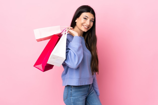 Joven morena sobre rosa aislado sosteniendo bolsas de compras y sonriendo