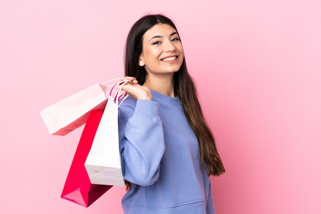 Joven morena sobre rosa aislado sosteniendo bolsas de compras y sonriendo