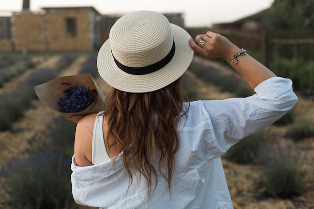 Joven morena con sombrero de paja mira a lo lejos contra el fondo de la floreciente lavanda joven