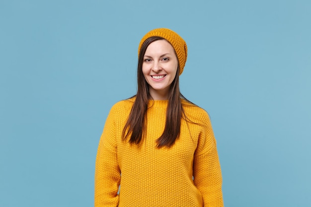 Una joven morena sonriente con suéter amarillo y sombrero posando aislada en un retrato de estudio de fondo de pared azul. Gente emociones sinceras concepto de estilo de vida. Simulacros de espacio de copia. Mirando la cámara.