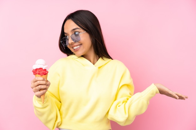 Joven morena sosteniendo un helado de cucurucho sobre pared rosa aislada sosteniendo copyspace con dos manos