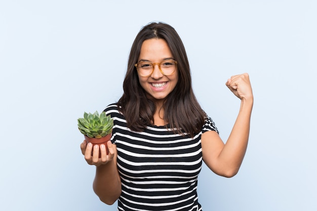 Joven morena sosteniendo una planta celebrando una victoria