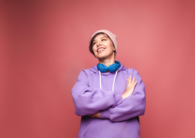 Joven morena con un suéter lila y auriculares posa aislada sobre un fondo rosa en el estudio El concepto del estilo de vida de las personas Escuchar música con auriculares retrato de estudio de baile