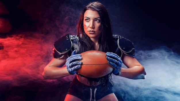 Joven morena con uniforme sexy de jugador de rugby posando con pelota.