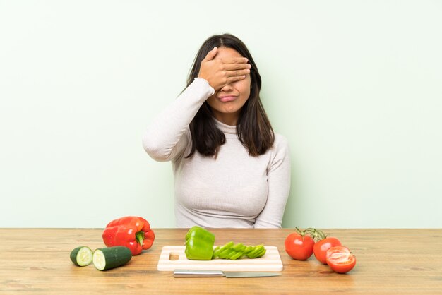 Joven morena con verduras cubriendo los ojos con las manos