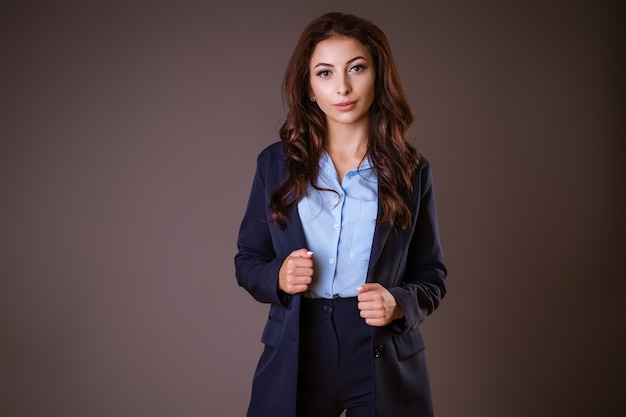 Una joven morena, vestida con un traje clásico, se aferra a su chaqueta, creando solidez contra un oscuro.