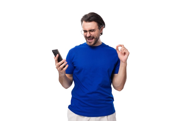 Foto un joven moreno bien arreglado con barba en una camiseta ve un video en un teléfono inteligente