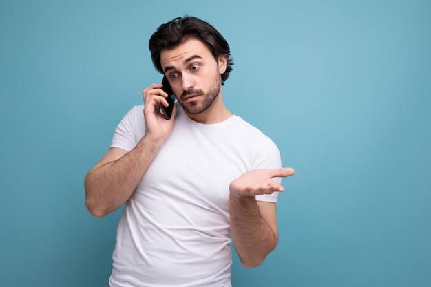 Un joven moreno con una camiseta blanca con un teléfono inteligente se comunica con un amigo