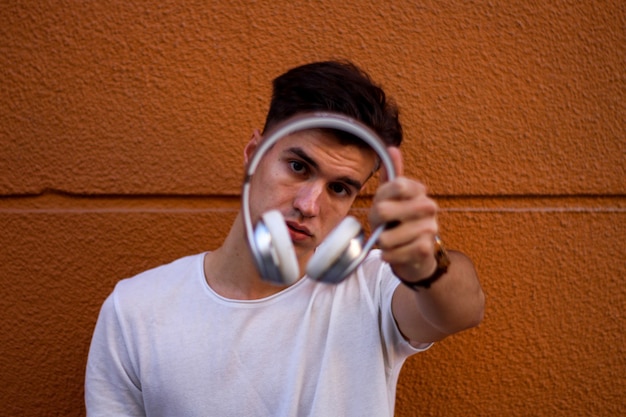 Joven mostrando auriculares sobre fondo naranja