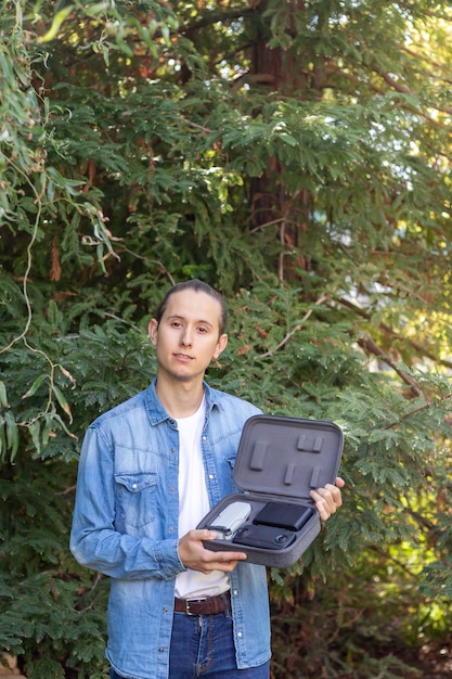 Joven mostrando un dron de última generación a la cámara en su maletín portátil en medio de la naturaleza