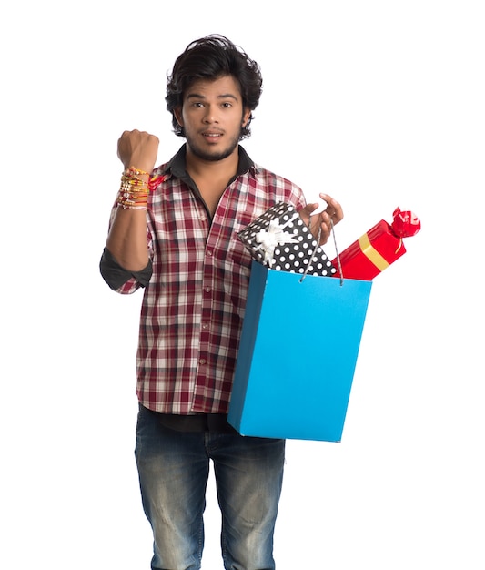 Joven mostrando rakhi en su mano con bolsas de compras y caja de regalo con motivo del festival Raksha Bandhan.