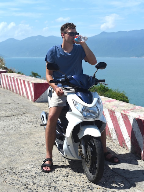 Joven un motociclista bebiendo agua de una botella de plástico