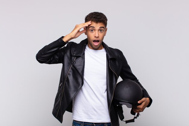 Joven motociclista que parece feliz, asombrado y sorprendido, sonriendo y dándose cuenta de buenas e increíbles noticias.