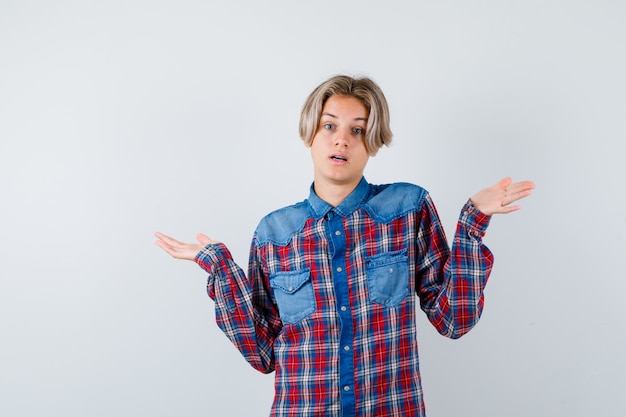 Joven muchacho adolescente en camisa a cuadros mostrando gesto de impotencia y mirando desconcertado