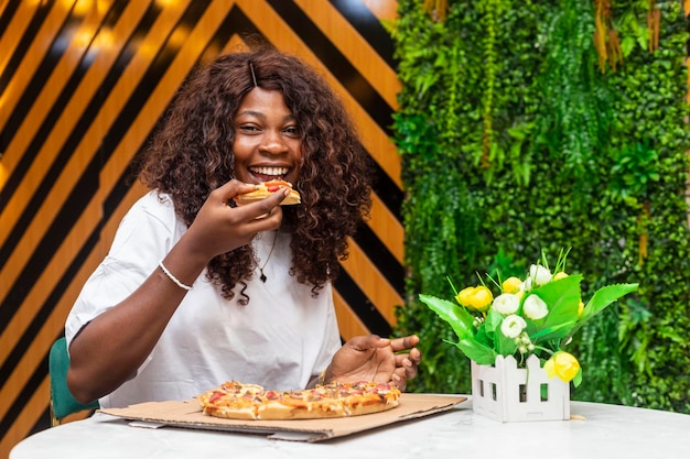 Joven mujer africana negra comiendo y sonriendo mirando a la cámara