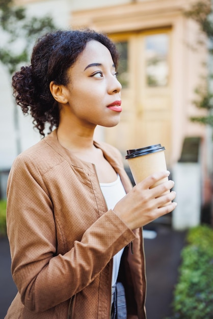 Joven mujer africana de raza mixta sosteniendo una taza de café de papel desechable en la calle