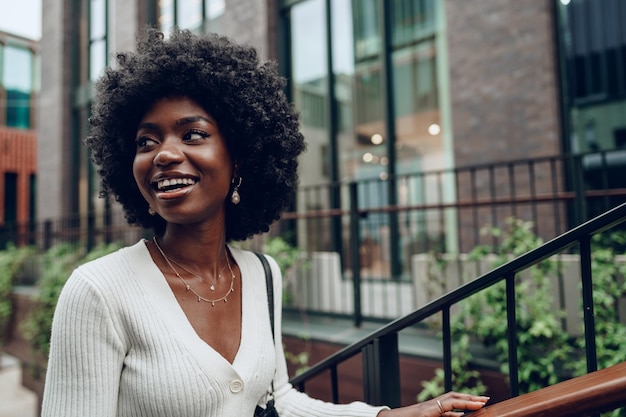 Joven mujer africana sonriente posa cerca de las escaleras en la ciudad