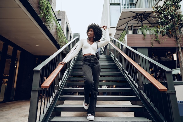 Joven mujer africana sonriente posa cerca de las escaleras en la ciudad