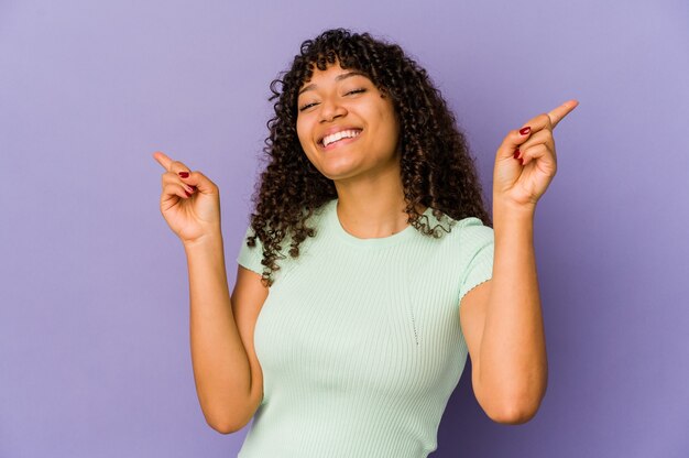 Joven mujer afro aislada apuntando a diferentes espacios de copia, eligiendo uno de ellos, mostrando con el dedo