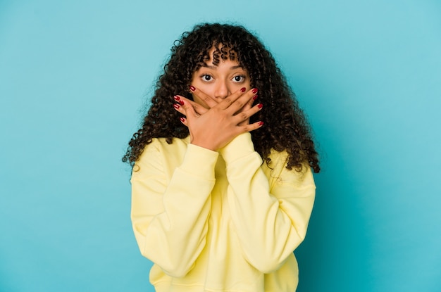 Joven mujer afro americana afro aislada conmocionado cubriendo la boca con las manos.