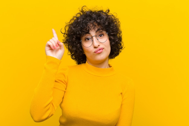 Foto joven mujer afro bonita que se siente como un genio sosteniendo el dedo con orgullo en el aire después de darse cuenta de una gran idea, diciendo eureka