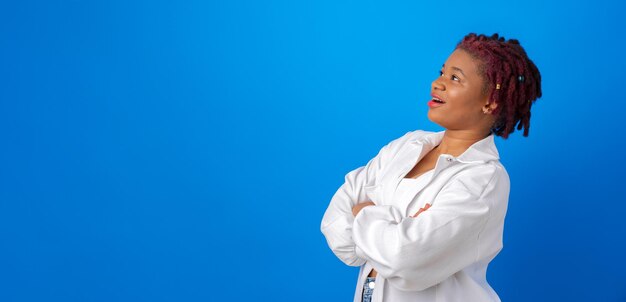 Joven mujer afro con camisa blanca mirando hacia arriba en el espacio de la copia para publicidad sobre fondo azul.