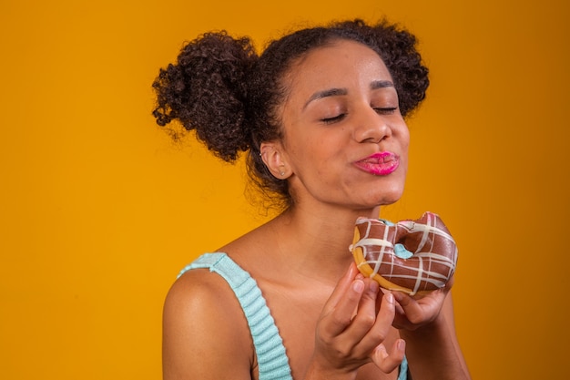 Joven mujer afro comiendo deliciosas donas de chocolate.