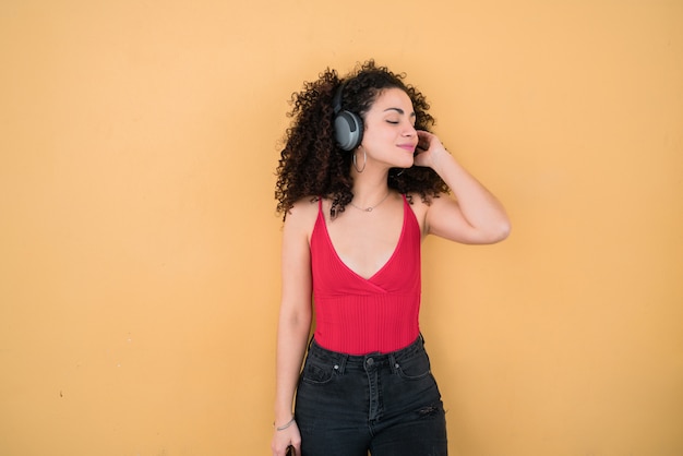 Joven mujer afro escuchando música con auriculares.