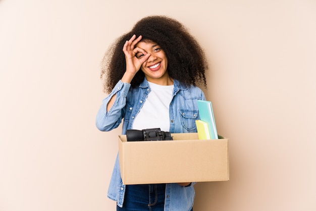 Joven mujer afro mudarse a casa Joven mujer afro emocionada manteniendo gesto bien en el ojo.