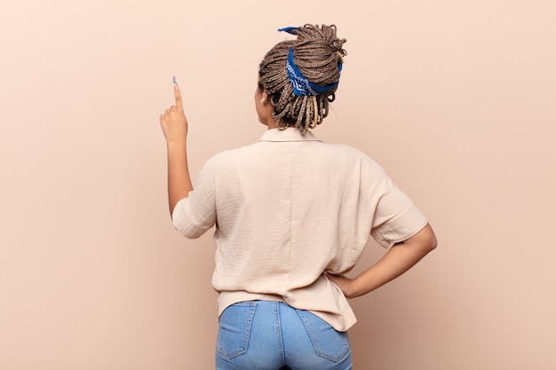 Foto joven mujer afro de pie y apuntando al objeto en el espacio de la copia, vista trasera