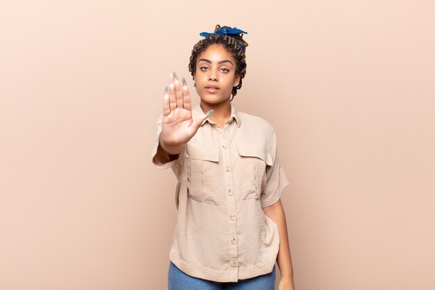 Joven mujer afro que parece seria, severa, disgustada y enojada mostrando la palma abierta haciendo gesto de parada
