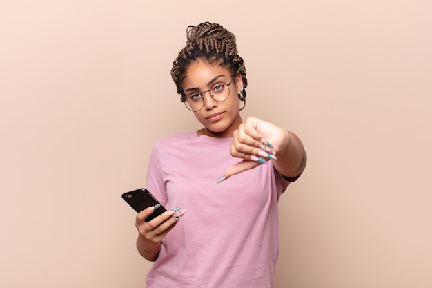 Joven mujer afro que se siente cruzada, enojada, molesta, decepcionada o disgustada, mostrando los pulgares hacia abajo