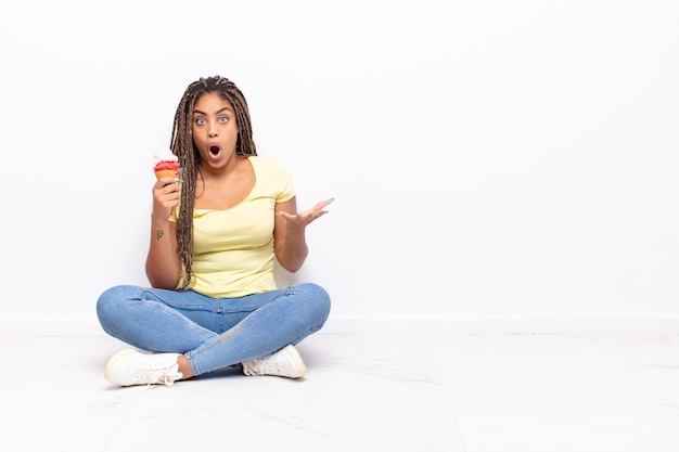 Joven mujer afro que se siente extremadamente conmocionada y sorprendida, ansiosa y en pánico, con una mirada estresada y horrorizada. concepto de helado