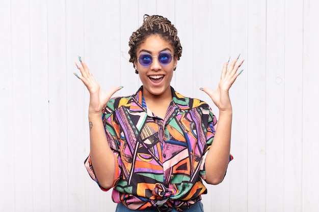 Joven mujer afro que se siente feliz, asombrada, afortunada y sorprendida, celebrando la victoria con ambas manos en el aire