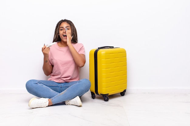 Joven mujer afro que se siente feliz, emocionada y positiva, dando un gran grito con las manos al lado de la boca, gritando. concepto de vacaciones