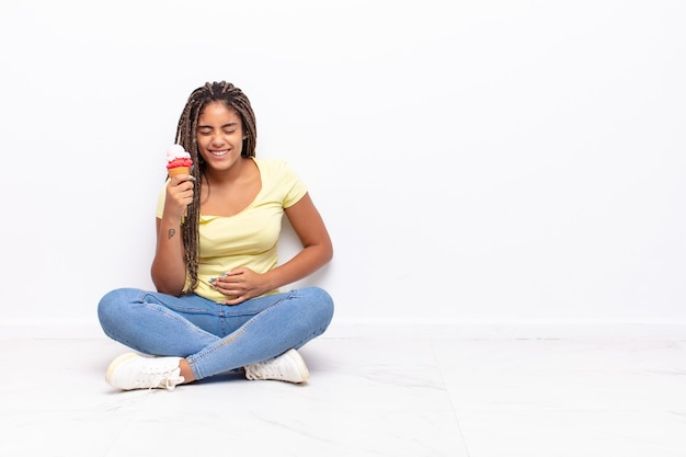 Joven mujer afro riéndose a carcajadas de una broma hilarante, sintiéndose feliz y alegre, divirtiéndose. concepto de helado