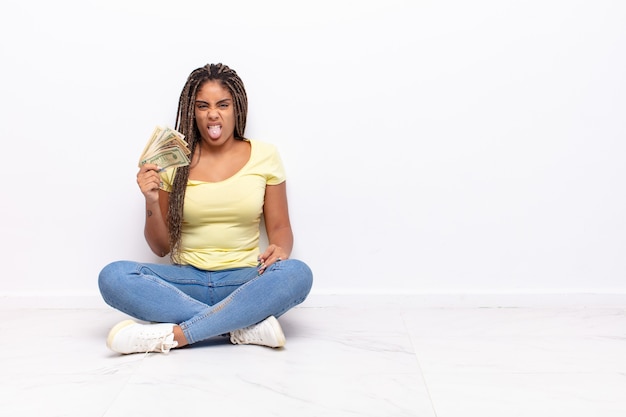 Joven mujer afro sintiéndose disgustada e irritada, sacando la lengua, disgustando algo desagradable y asqueroso. concepto de dinero