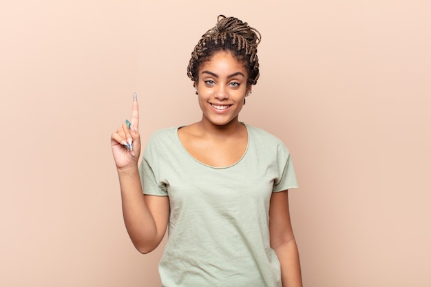 Joven mujer afro sonriendo alegre y felizmente, apuntando hacia arriba