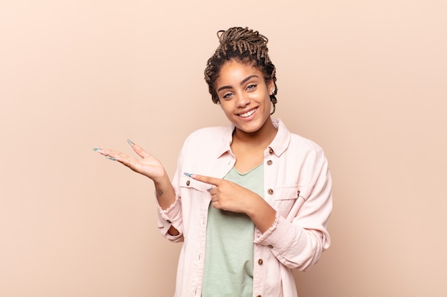 Joven mujer afro sonriendo alegremente y apuntando al espacio de la copia en la palma lateral, mostrando o publicitando un objeto