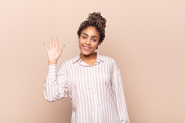 Joven mujer afro sonriendo feliz y alegremente, agitando la mano