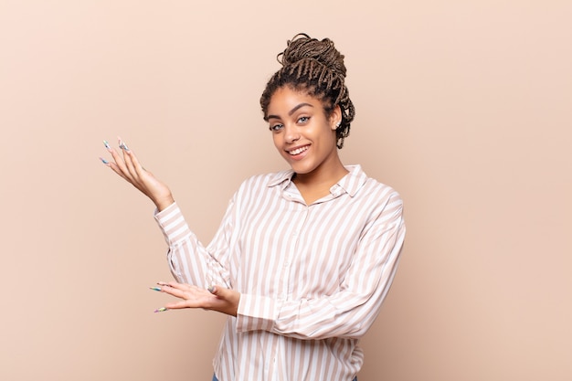 Joven mujer afro sonriendo con orgullo y confianza, sintiéndose feliz y satisfecha y mostrando un concepto