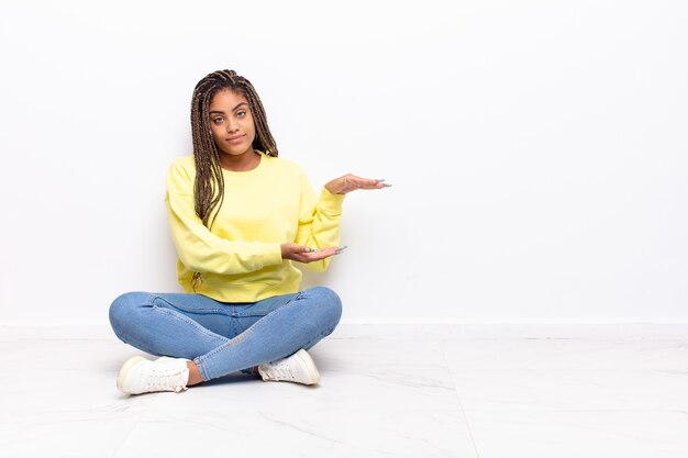 Joven mujer afro sosteniendo un objeto con ambas manos en el espacio de copia lateral, mostrando, ofreciendo o publicitando un objeto