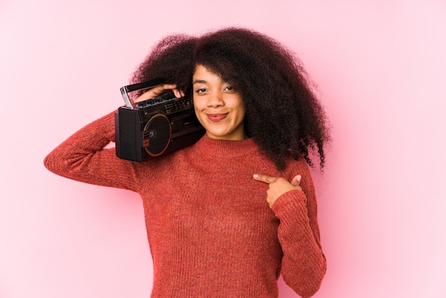 Joven mujer afro sosteniendo una persona aislada cassete apuntando con la mano a una camisa copia espacio, orgulloso y confiado