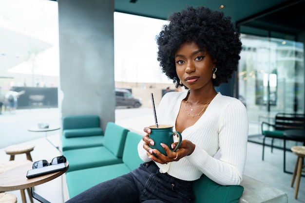 Joven mujer afro tomando un descanso y bebiendo café en la cafetería