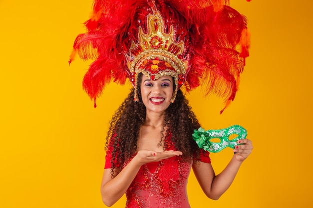 Joven mujer afro en traje de samba y carnaval sosteniendo una máscara verde sonriendo a la cámara.