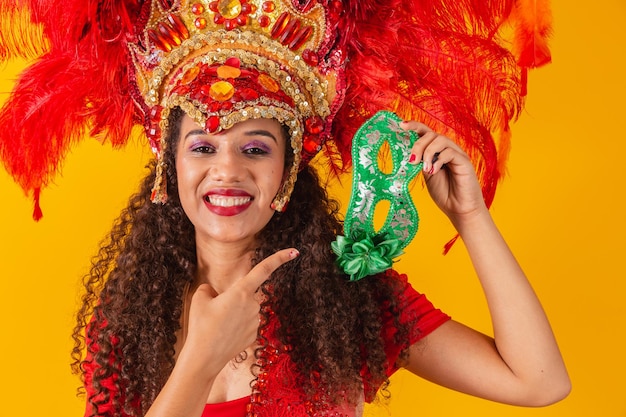 Joven mujer afro en traje de samba y carnaval sosteniendo una máscara verde sonriendo a la cámara.