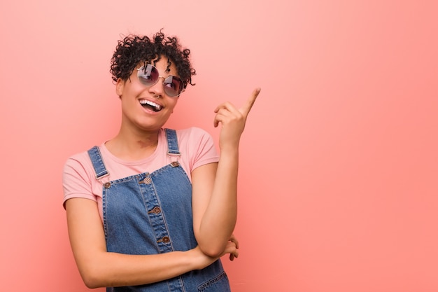 Joven mujer afroamericana adolescente mixta sonriendo alegremente señalando con el dedo lejos.