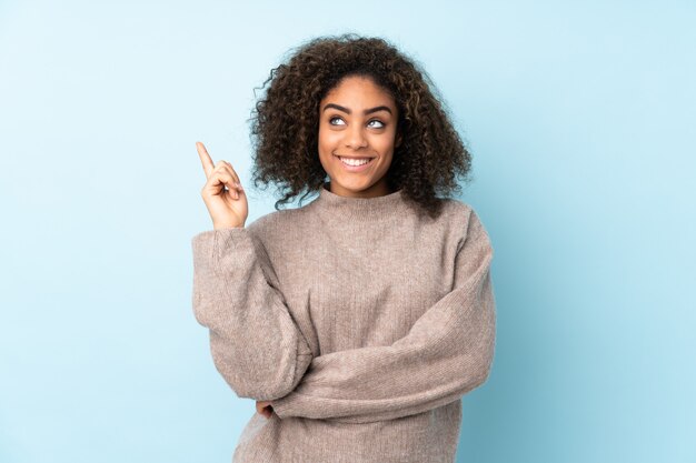 Joven mujer afroamericana aislada en azul apuntando una gran idea