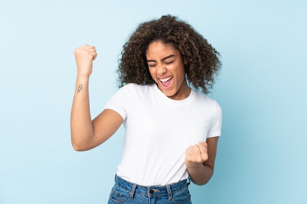 Joven mujer afroamericana aislada en azul celebrando una victoria